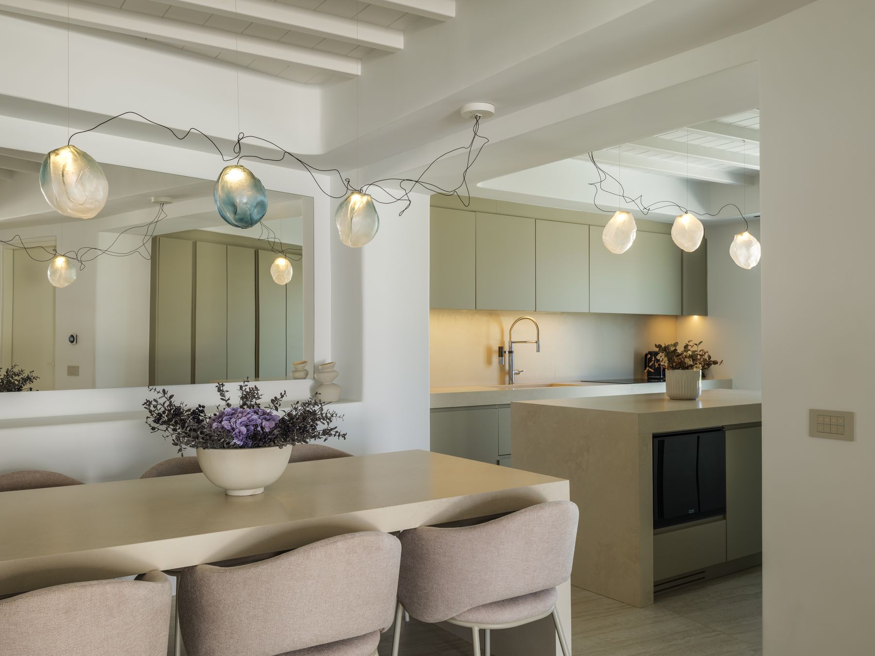 Dining table under Bocci pendant lights, with the kitchen behind